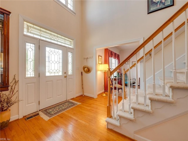 entryway with wood finished floors, a towering ceiling, visible vents, stairs, and baseboards