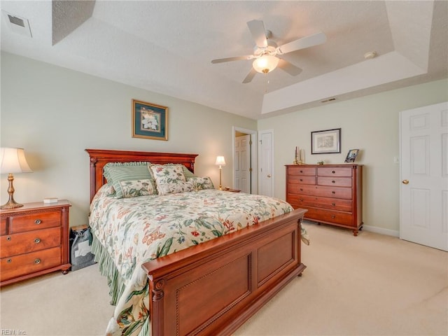 bedroom with a raised ceiling, light colored carpet, visible vents, a ceiling fan, and baseboards