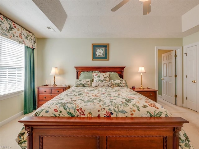 bedroom with a textured ceiling, light colored carpet, a ceiling fan, baseboards, and visible vents