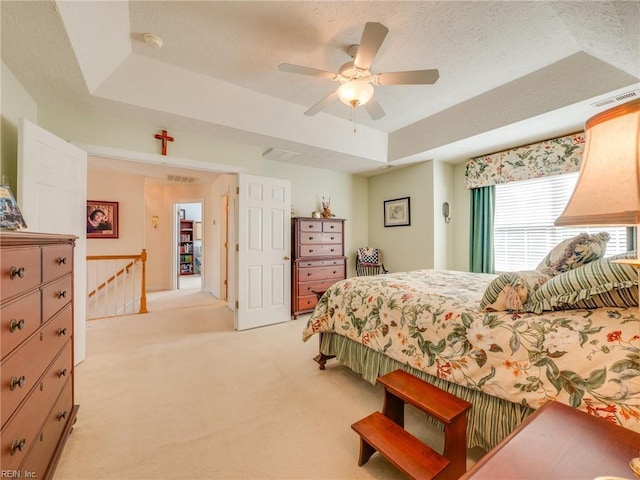 bedroom with a tray ceiling, visible vents, light carpet, ceiling fan, and a textured ceiling