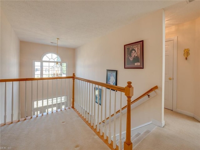 hallway with a textured ceiling, carpet, an inviting chandelier, and baseboards