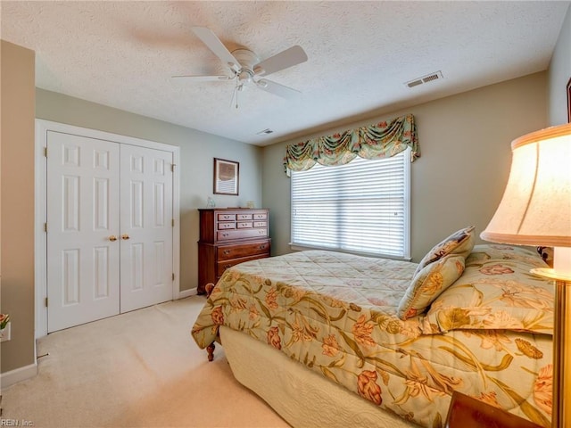 bedroom featuring a closet, light colored carpet, visible vents, a ceiling fan, and a textured ceiling