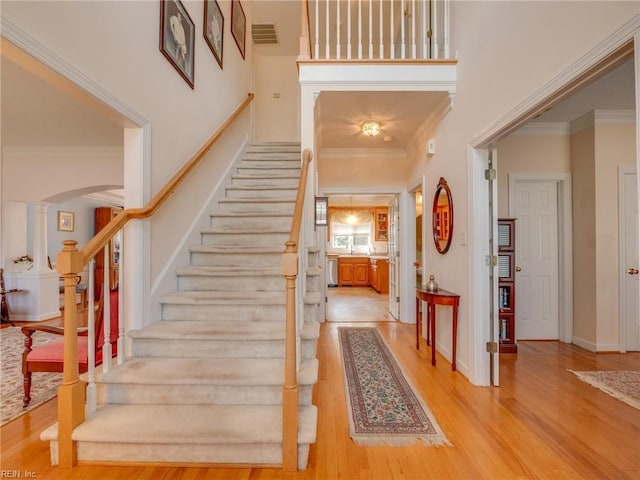 entryway with visible vents, crown molding, light wood-style flooring, and a high ceiling