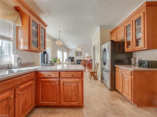 kitchen with brown cabinetry, glass insert cabinets, freestanding refrigerator, a peninsula, and light countertops