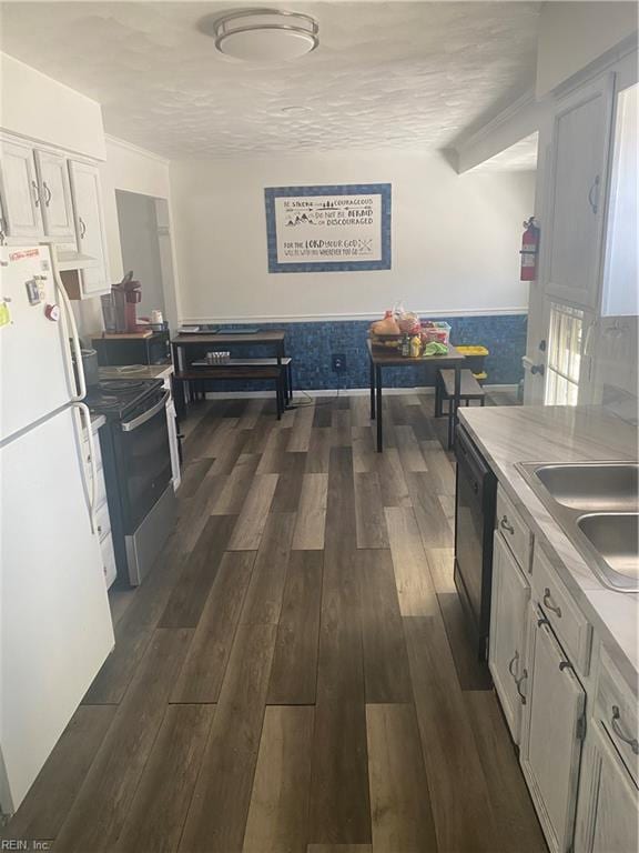 kitchen featuring dark wood-type flooring, a sink, black dishwasher, freestanding refrigerator, and stainless steel range with electric stovetop