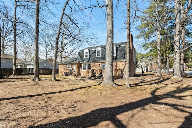 back of property with fence, a gambrel roof, and brick siding