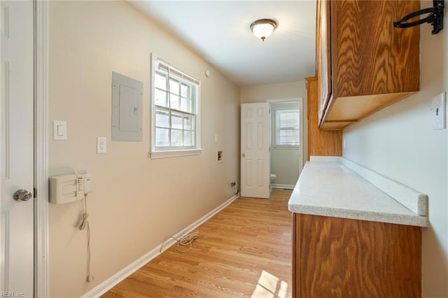 hall featuring light wood finished floors, electric panel, and baseboards