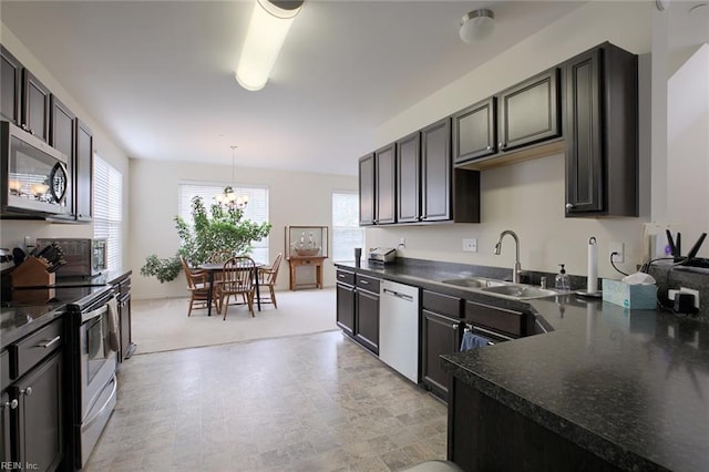 kitchen featuring decorative light fixtures, a notable chandelier, stainless steel appliances, dark countertops, and a sink