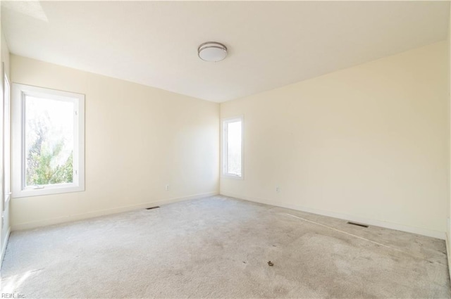 empty room featuring light carpet, visible vents, and baseboards