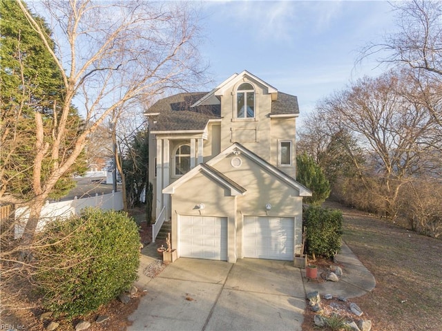 view of front of home with concrete driveway, roof with shingles, an attached garage, fence, and stucco siding