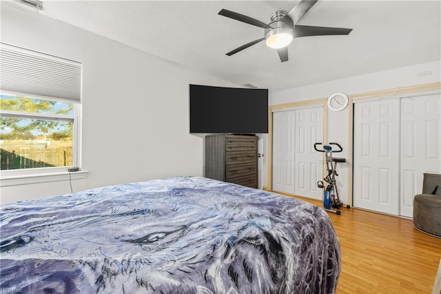 bedroom with two closets, lofted ceiling, a ceiling fan, a textured ceiling, and wood finished floors