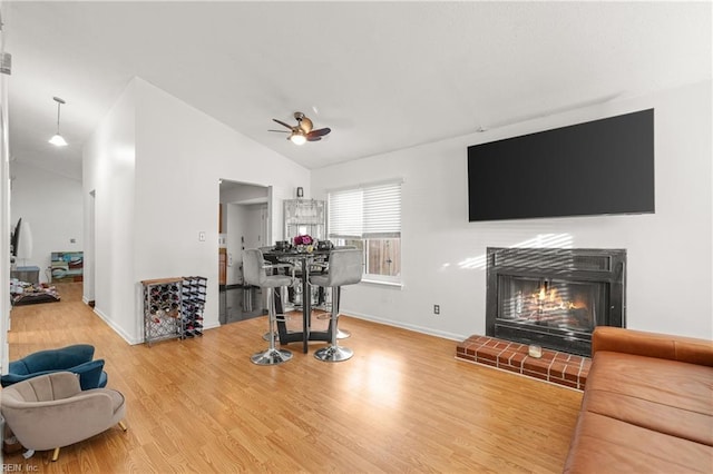 living room with ceiling fan, lofted ceiling, wood finished floors, baseboards, and a brick fireplace