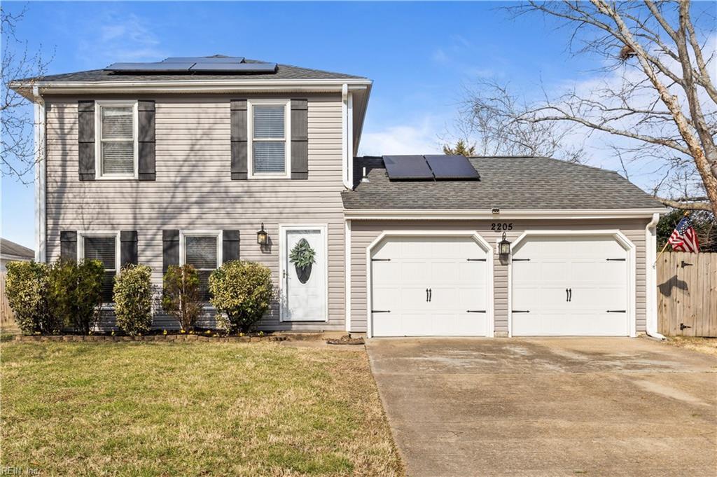 view of front of house with a garage, driveway, a front yard, and solar panels