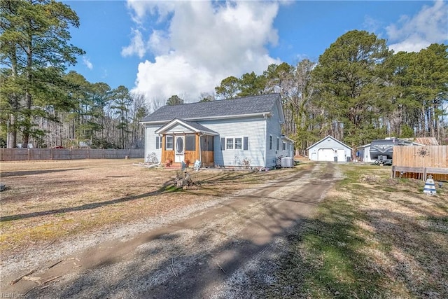 view of front facade featuring an outbuilding, a detached garage, dirt driveway, central air condition unit, and fence