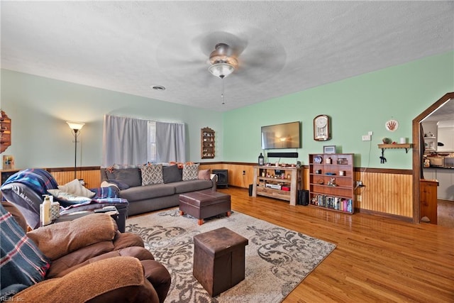 living area with a wainscoted wall, wood walls, a textured ceiling, and wood finished floors