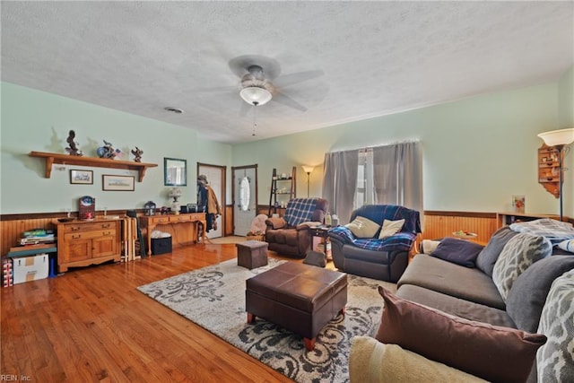 living area with wainscoting, wood walls, ceiling fan, a textured ceiling, and wood finished floors