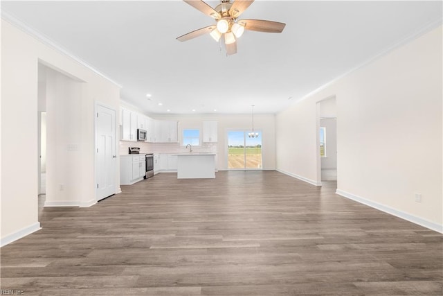 unfurnished living room with ceiling fan with notable chandelier, baseboards, crown molding, and wood finished floors