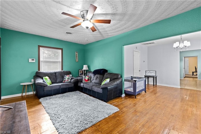 living area featuring baseboards, visible vents, wood finished floors, a textured ceiling, and ceiling fan with notable chandelier