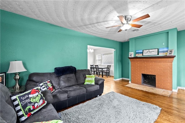 living room featuring ceiling fan with notable chandelier, a brick fireplace, wood finished floors, and visible vents