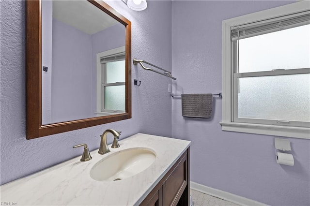 bathroom with a textured wall, baseboards, and vanity