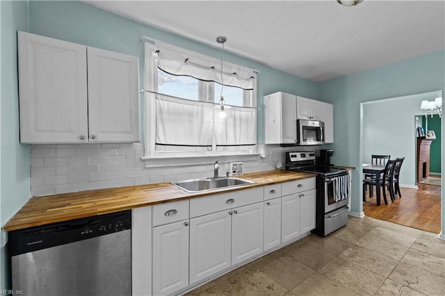 kitchen featuring stainless steel appliances, butcher block counters, a sink, white cabinetry, and backsplash