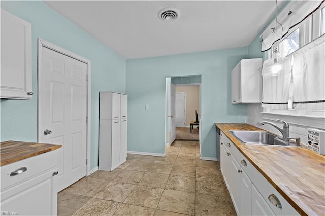 kitchen featuring butcher block countertops, visible vents, white cabinets, and a sink