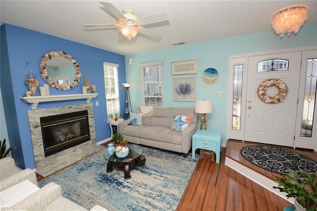 living area with a stone fireplace, wood finished floors, visible vents, baseboards, and a ceiling fan