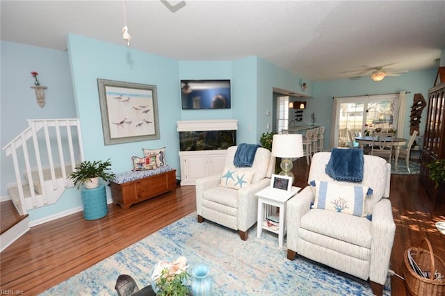 living area with a ceiling fan, stairs, baseboards, and wood finished floors