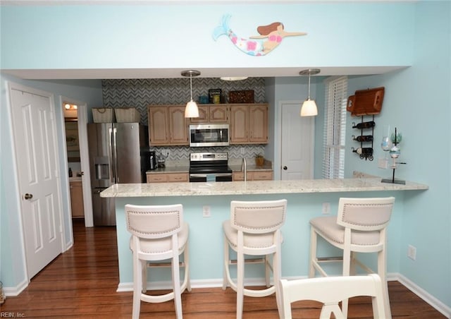 kitchen with tasteful backsplash, hanging light fixtures, appliances with stainless steel finishes, dark wood-type flooring, and a kitchen breakfast bar