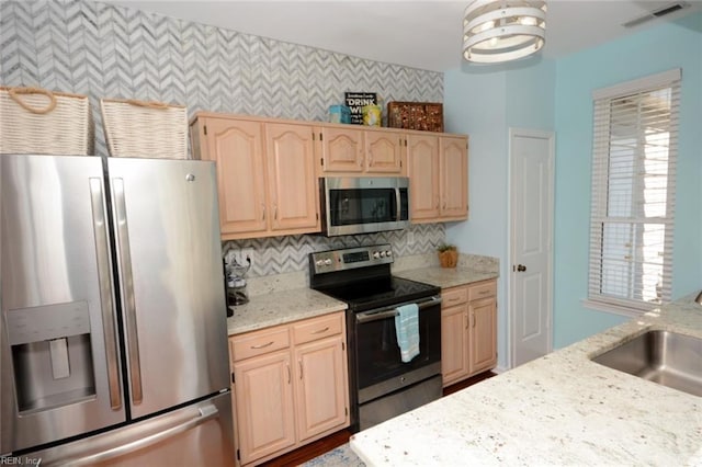 kitchen featuring stainless steel appliances, visible vents, light brown cabinets, a sink, and light stone countertops