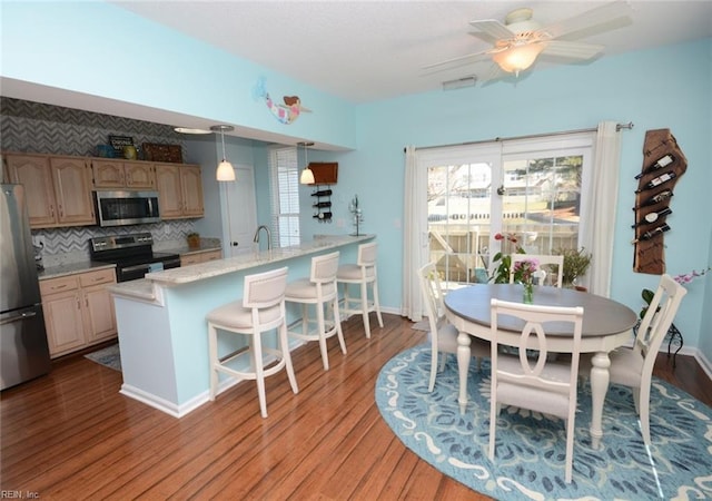 kitchen featuring backsplash, appliances with stainless steel finishes, wood finished floors, a peninsula, and a kitchen breakfast bar