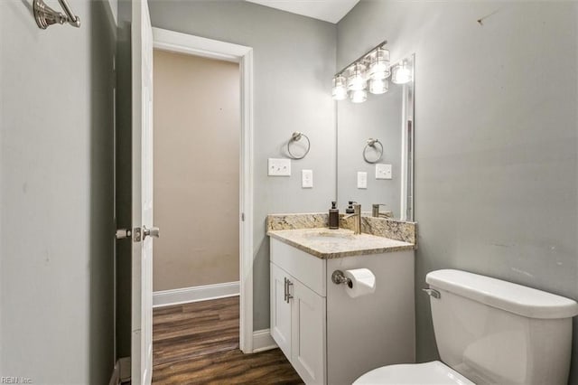 bathroom featuring toilet, baseboards, wood finished floors, and vanity