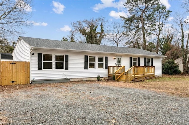 ranch-style home featuring roof with shingles, driveway, a wooden deck, and fence