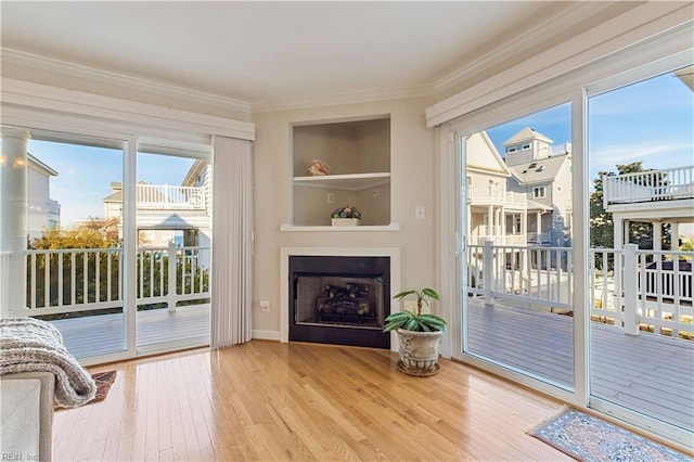 doorway to outside featuring built in features, wood-type flooring, a fireplace, and crown molding