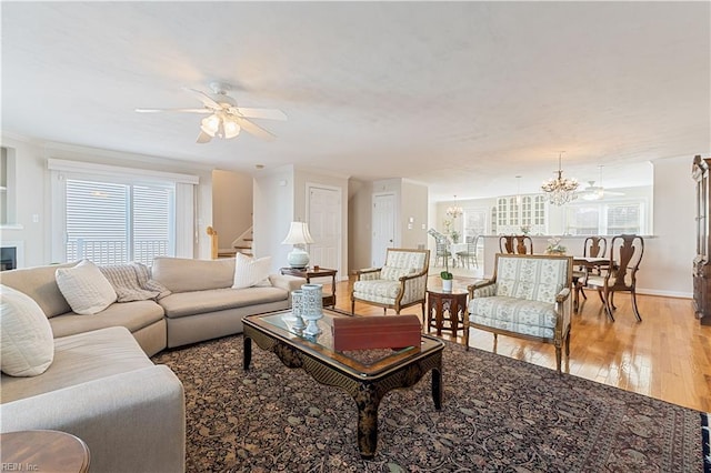 living area with hardwood / wood-style flooring, ceiling fan with notable chandelier, baseboards, ornamental molding, and stairway