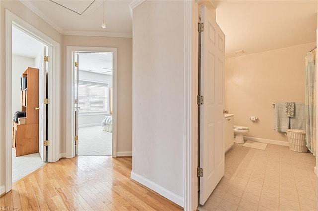 hallway with light wood-type flooring, baseboards, ornamental molding, and attic access