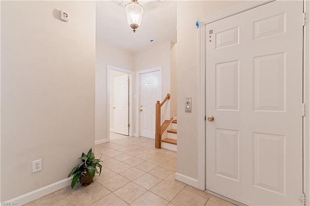 corridor featuring light tile patterned floors, baseboards, and stairs