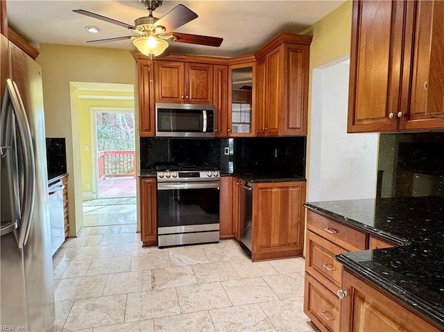 kitchen featuring tasteful backsplash, brown cabinetry, ceiling fan, appliances with stainless steel finishes, and dark stone countertops