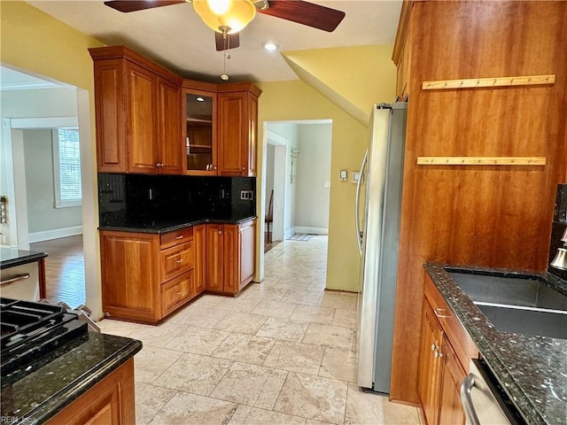 kitchen with dark stone counters, stainless steel appliances, tasteful backsplash, and brown cabinets