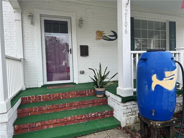 view of exterior entry featuring covered porch and brick siding