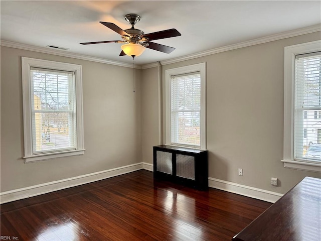 empty room featuring wood finished floors, a ceiling fan, visible vents, baseboards, and ornamental molding