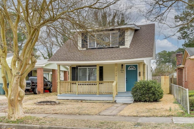 view of front of home with covered porch, brick siding, roof with shingles, and fence