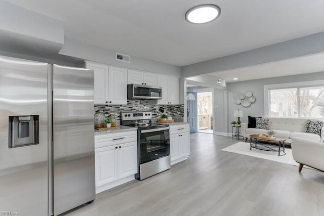 kitchen with white cabinets, visible vents, stainless steel appliances, and backsplash