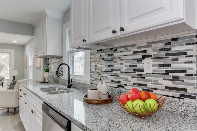 kitchen featuring a sink, white cabinets, stainless steel dishwasher, light stone countertops, and tasteful backsplash