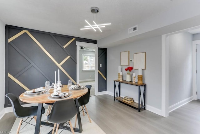 dining room featuring ceiling fan with notable chandelier, visible vents, baseboards, and wood finished floors