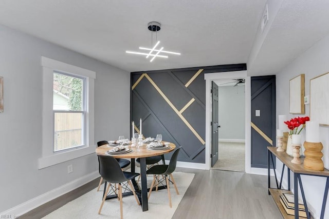 dining room featuring a textured ceiling, ceiling fan with notable chandelier, wood finished floors, and baseboards