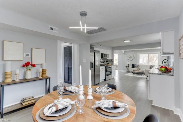 dining space with light wood finished floors, visible vents, and baseboards