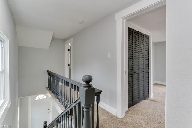 corridor featuring carpet floors, baseboards, and an upstairs landing