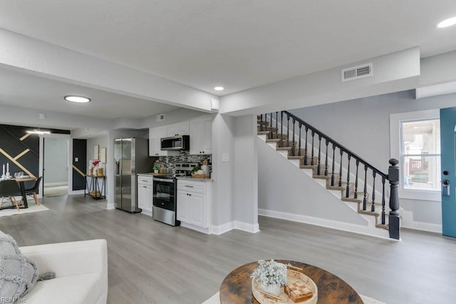 living area with baseboards, visible vents, stairway, and light wood finished floors