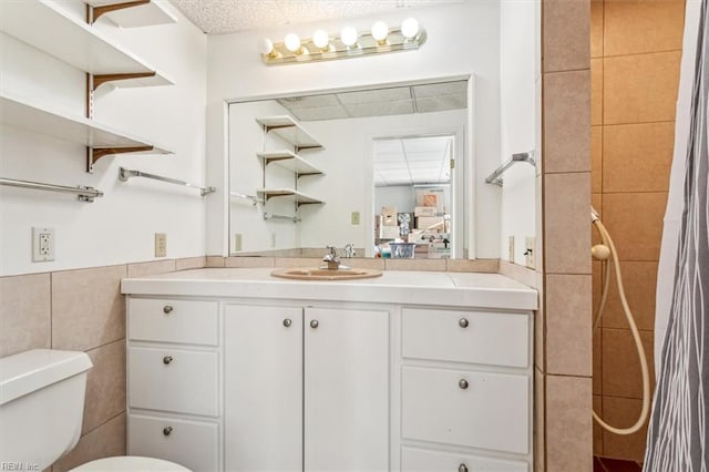 bathroom with toilet, a tile shower, tile walls, and vanity